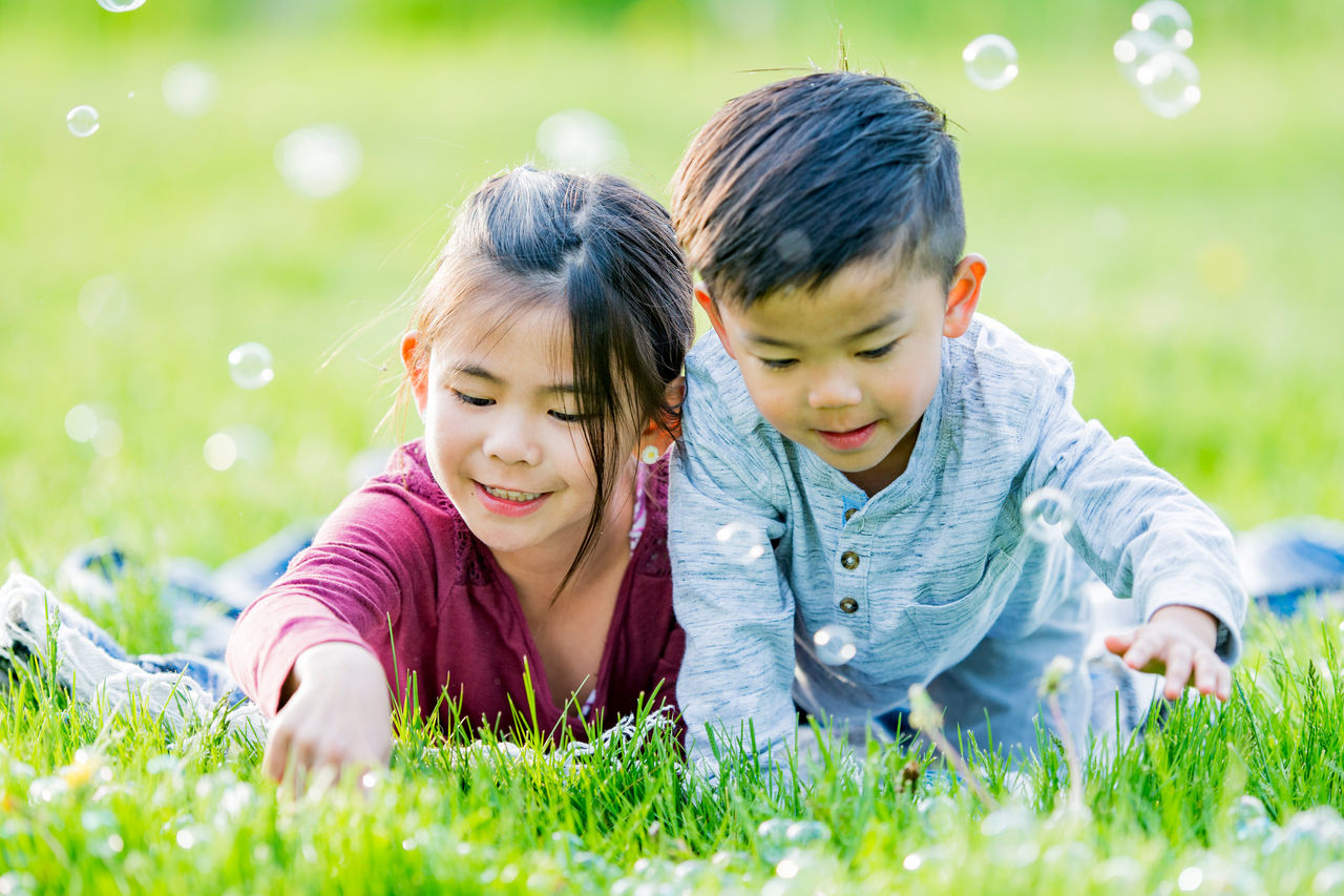 siblings laying in grass with bubbles