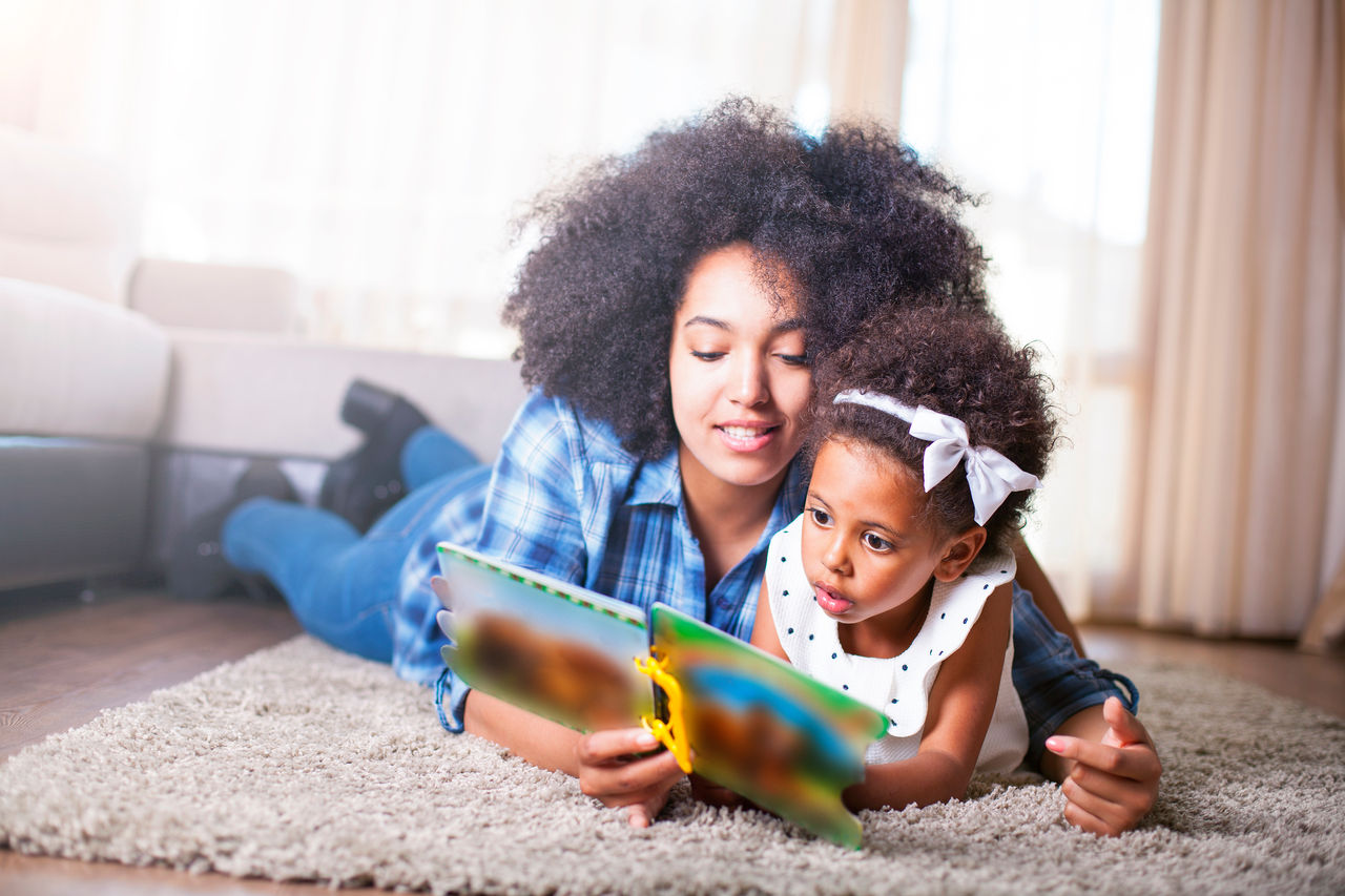 A mother laying on the floor reading with her 3 year old.