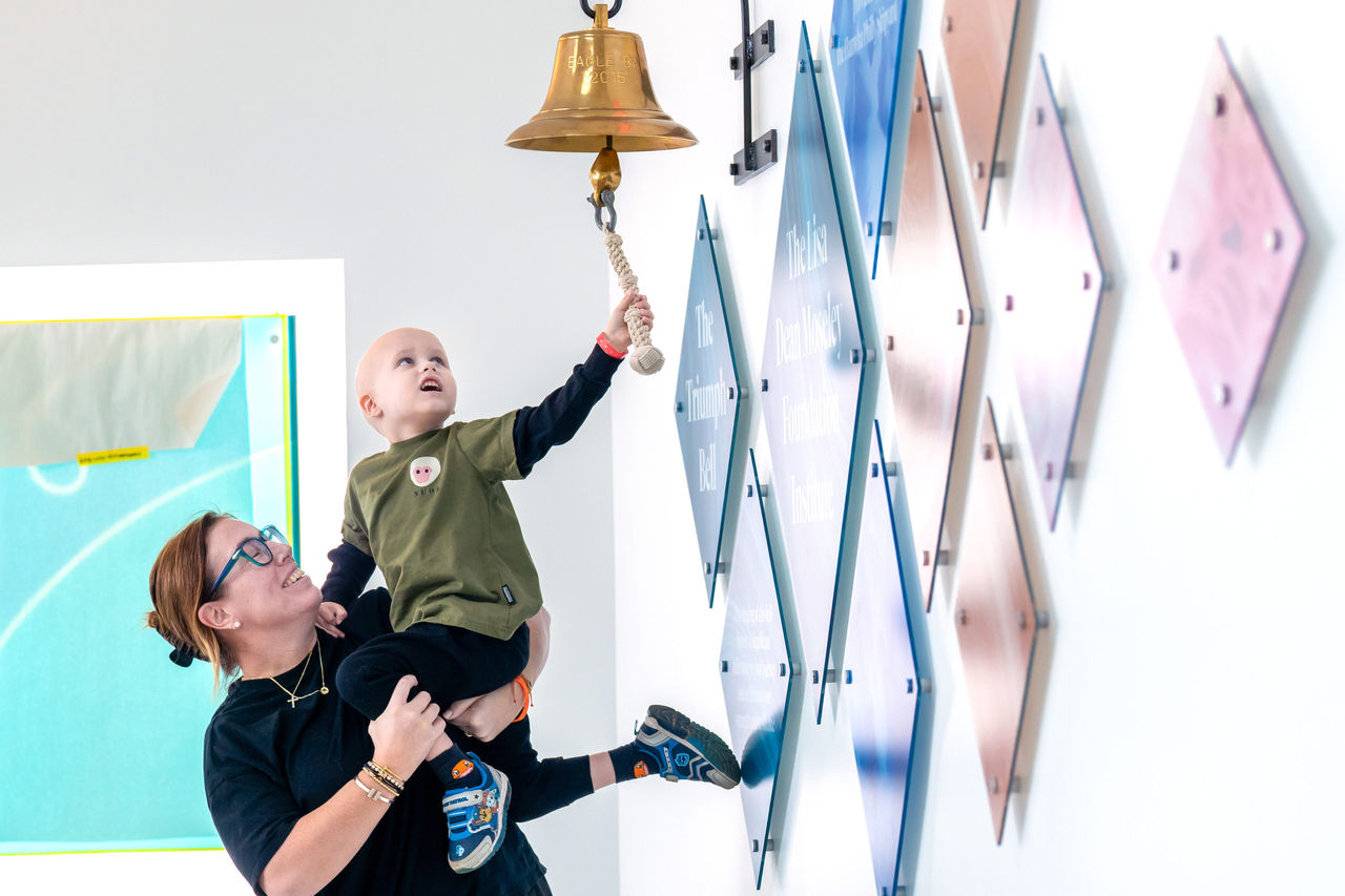 A child being lifted up to ring the cancer bell