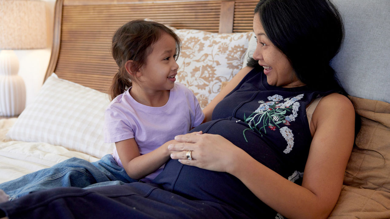 Young Girl Touches Pregnant Woman’s Belly on Bed